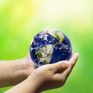 Photo of a globe in the hands of two people, against a green background.