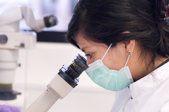 Understand Infections Wissenschaftlerin mit Mundschutz am Mikroskop