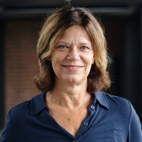 Das Portraitfoto zeigt eine Forscherin mit halblangen braunen Haaren, sie trägt eine dunkelblaue Bluse.