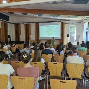 LCI Summer School 2026 Das Foto zeigt einen Raum, in dem die Studierenden auf Holzstühlen sitzen. Das Foto ist von hinten im Raum aufgenommen - die Personen sind mit dem Rücken zu sehen. Vorne ist eine Leinwand.