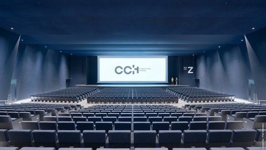 Das Foto zeigt einen leeren Kongressaal von hinten/ oben. Vorne an der Leinwand steht "CCH".