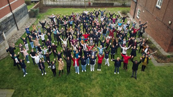 The photo shows the employees from above in the institute's garden. They are holding their arms up in the air.