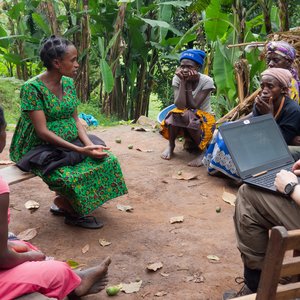 A group of people are sitting in a circle with Fabien Schultz, taking part in a community discussion. They are outdoors, with trees in the background. Fabien Schultz has his laptop on his lap.