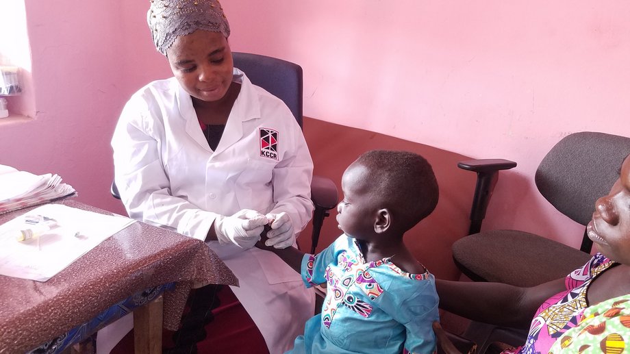 Untersuchung auf Malaria-Infektionen einer Kinderambulanz Eine KCCR-Mitarbeiterin nimmt Blut an der Fingerkuppe eines Kleinkindes ab, um es auf Malaria zu testen.