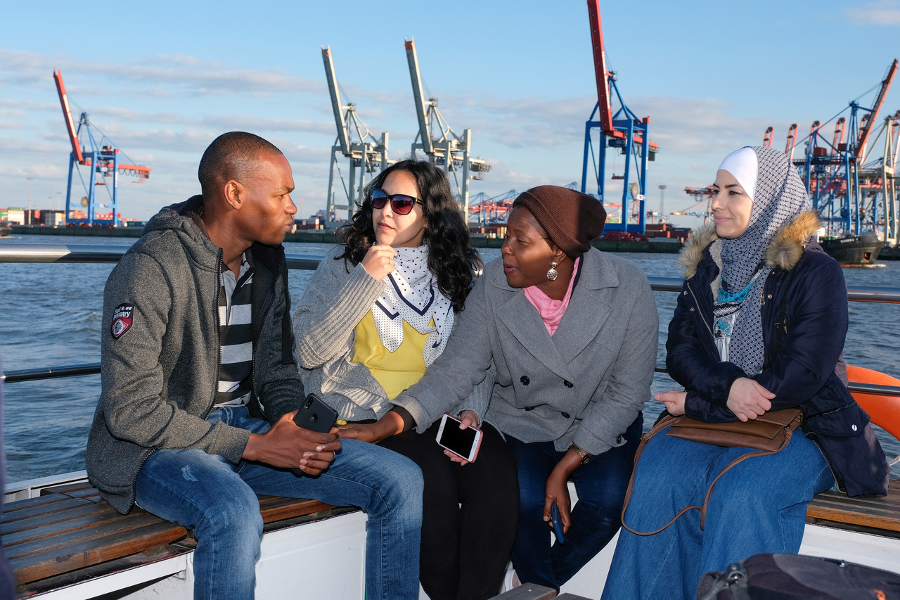 Das Foto zeigt vier Personen auf einem Boot im Hambuger Hafen, im Hintergrund sind die Hafenkräne zu sehen.